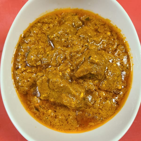 A white bowl filled with a rich, orange-brown Indian curry, featuring chunks of meat or paneer.