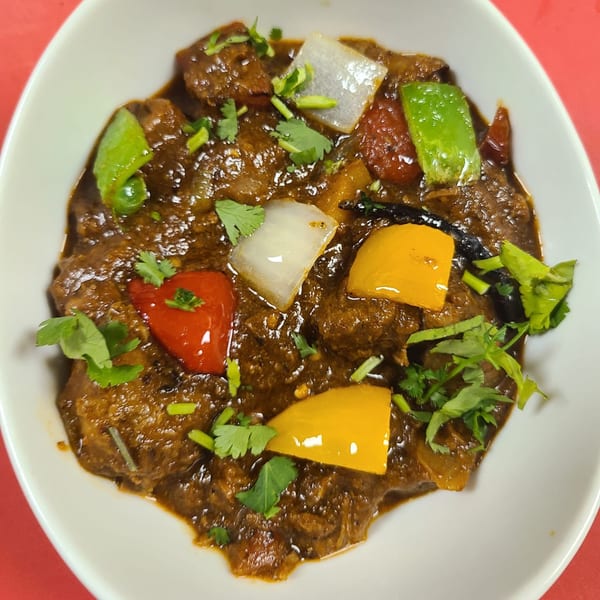 Indian curry with meat, bell peppers, onions, and cilantro in a white bowl.