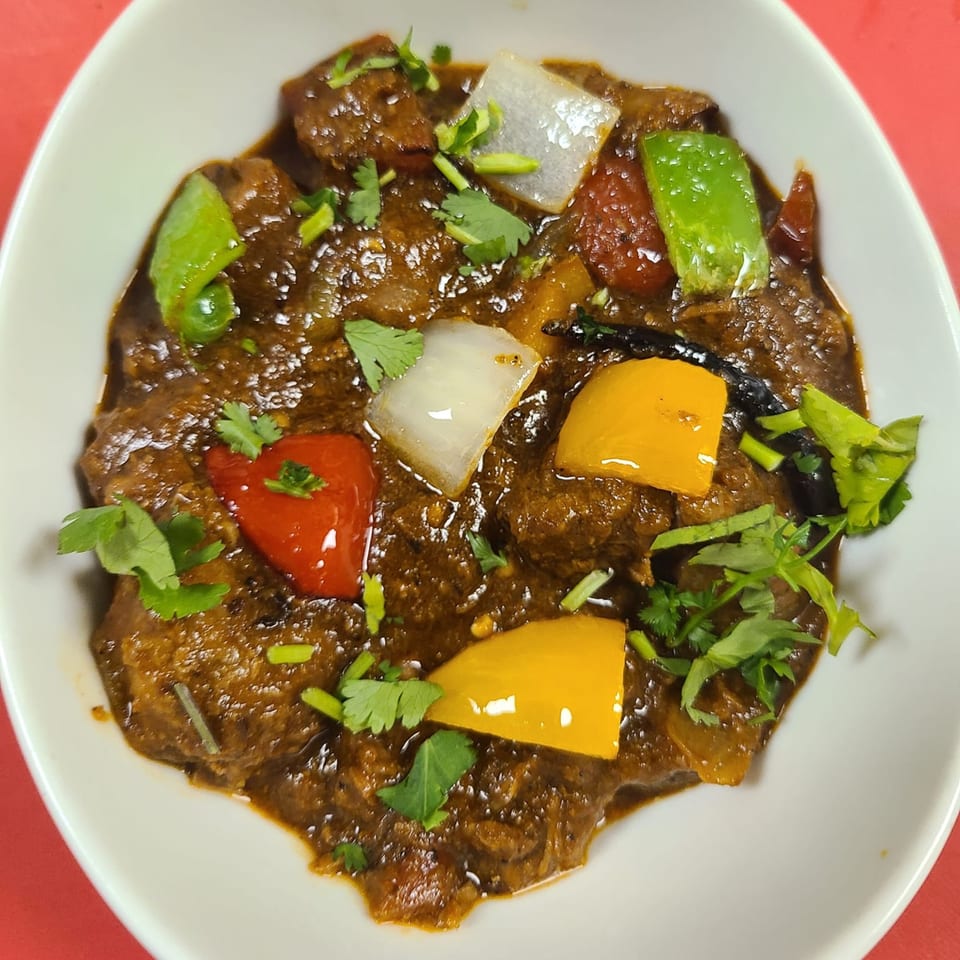 Indian curry with meat, bell peppers, onions, and cilantro in a white bowl.