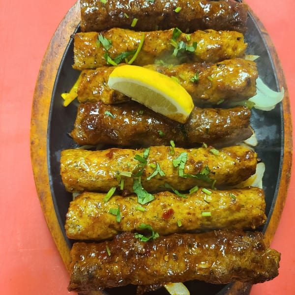 Sizzling Indian kebabs, garnished with cilantro and a lemon wedge, on a black platter.
