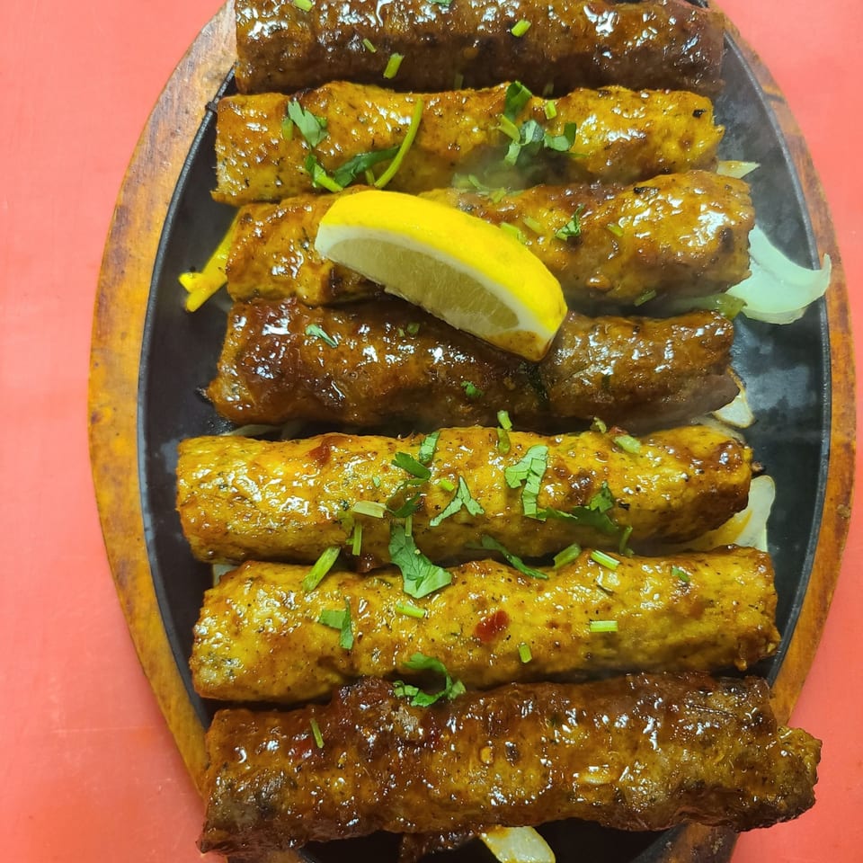 Sizzling Indian kebabs, garnished with cilantro and a lemon wedge, on a black platter.