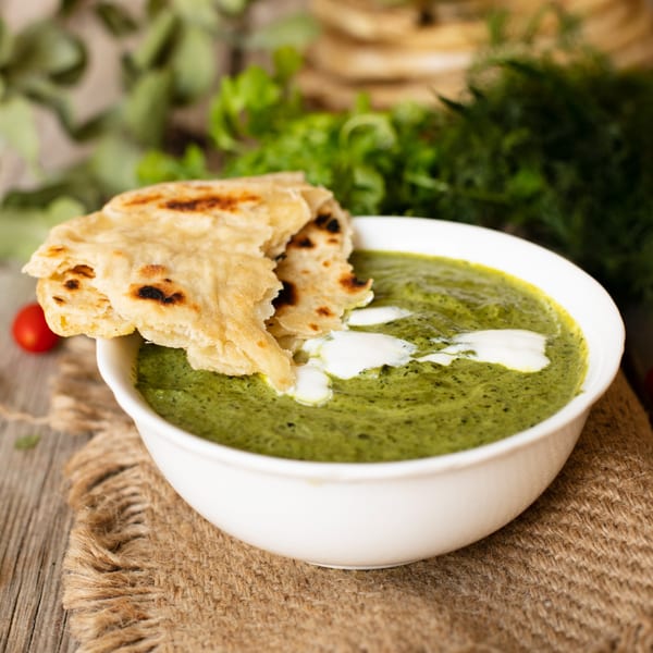 New Little India's vibrant green Indian curry with cream swirls, served with warm flatbread on a rustic table.