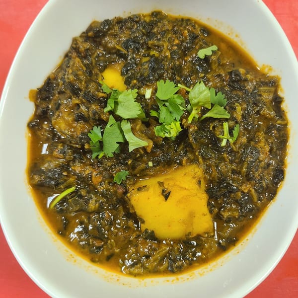 A white bowl filled with New Little India's Saag Aloo, garnished with fresh cilantro.