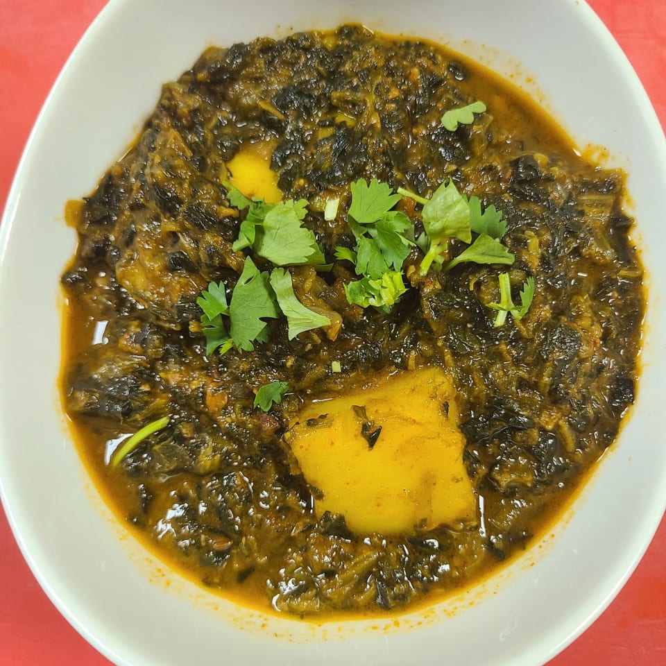 A white bowl filled with New Little India's Saag Aloo, garnished with fresh cilantro.